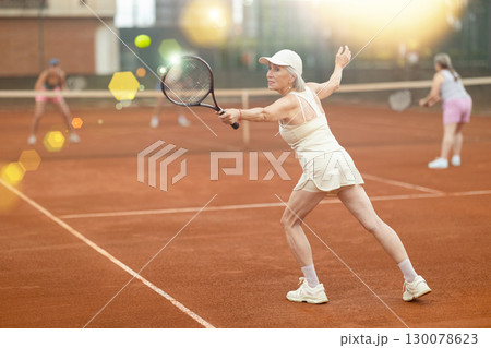 Elderly woman engrossed in tennis game on clay court 130078623