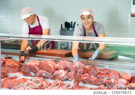 Adult man and young woman sellers lay out beef in butcher shop Adult man and young woman sellers lay out beef in butcher shop 130078672