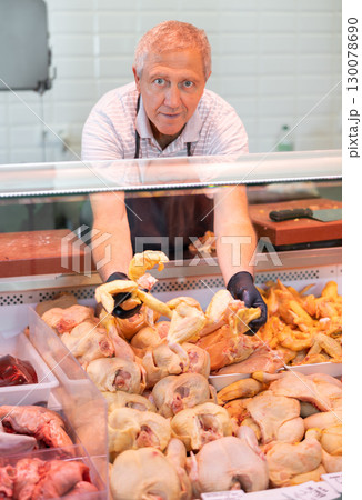 Adult man seller lays out chicken in butcher shop 130078690