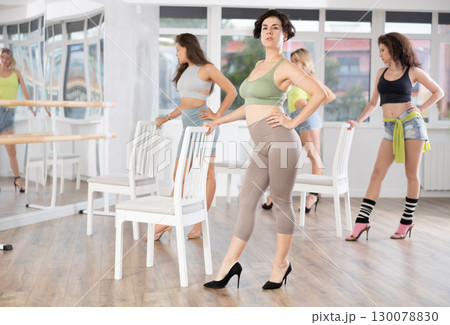 Active female dancer with group of women of different ages practicing strip plastic movements near chair in training hall during dancing classes 130078830
