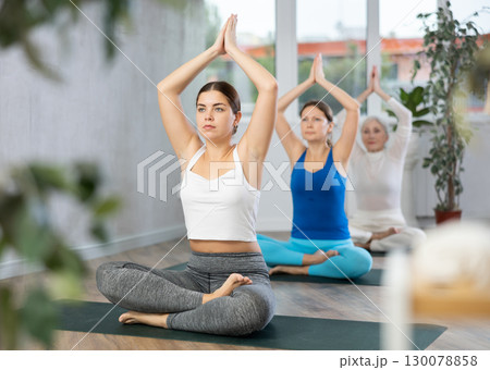 Happy positive women exercising yoga poses in fitness yoga center Happy positive women exercising yoga poses in fitness yoga center 130078858