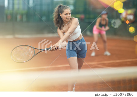 Two young women playing doubles tennis 130078860
