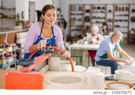 Young woman rolls out clay on craft machine clay press roller in studio 130078873