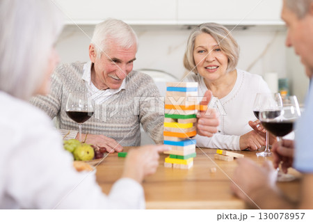 Group of four mature friends is playing board game with wooden blocks in kitchen Group of four mature friends is playing board game with wooden blocks in kitchen 130078957