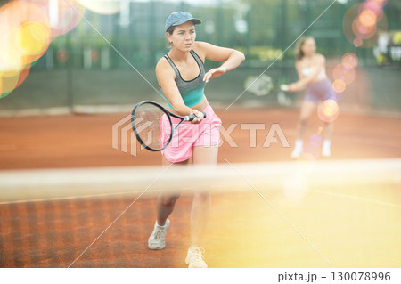 Two young women playing doubles tennis 130078996