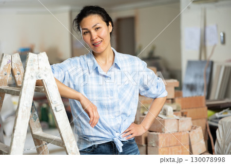 Portrait of a positive confident woman standing near a stepladder 130078998