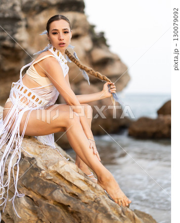 Girl on seashore in sexy and revealing carnival costume sitting on stone Girl on seashore in sexy and revealing carnival costume sitting on stone 130079092