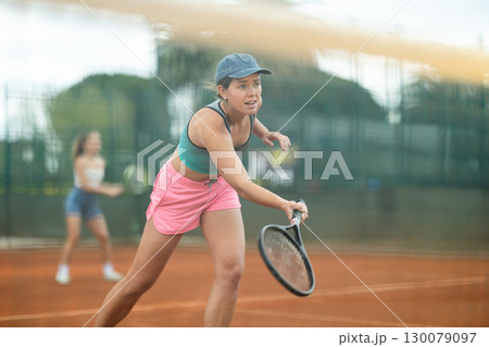 Two young women playing doubles tennis 130079097