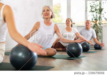 Group of mature active people doing soft ball exercises during group pilates class in fitness studio 130079098