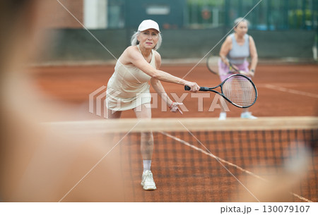 Elderly woman engrossed in doubles tennis game on clay court Elderly woman engrossed in doubles tennis game on clay court 130079107