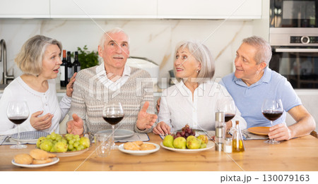 Group of happy elderly people drink red wine and chat at festive table 130079163