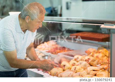 Senior man choosing raw meat in display case in butcher shop Senior man choosing raw meat in display case in butcher shop 130079241