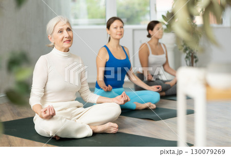 Mature female yoga instructor showing others yoga poses in wellness center Mature female yoga instructor showing others yoga poses in wellness center 130079269