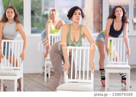 Group of girls unleash their energy and dance passionately near a chair in high heels in a dance studio. His powerful moves combined with elegance of high heels 130079389