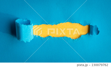 Hole ripped in blue paper on yellow background. 130079762