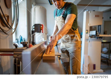 Skilled carpenter apply full attention to precision work on jointer machine processing wooden beam 130079795