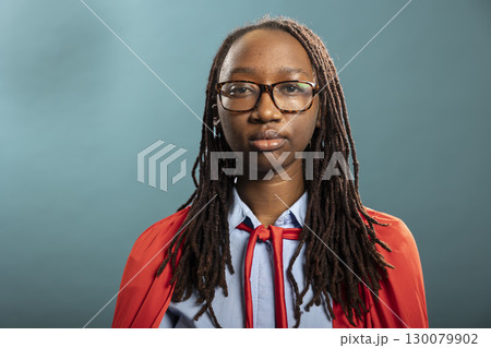 Closeup of black woman looking straight into camera, radiating confidence and empowerment in blue background studio. Her bold expression highlights strength, beauty and self assurance. 130079902