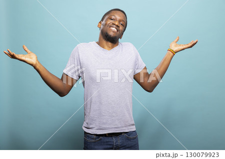 African american man standing and shrugging over an isolated background, expressing uncertainty. Young black male individual wearing casual clothing and looking at camera with open arms. African american man standing and shrugging over an isolated background, expressing uncertainty. Young black male individual wearing casual clothing and looking at camera with open arms. 130079923