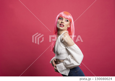 Glamourous woman posing with pink wig and off trendy blouse against isolated background. Vibrant fashion portrait of caucasian female model with playful energy and bold expression. 130080024