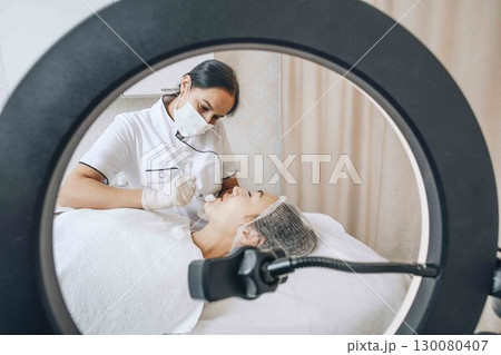 A cosmetologist blogger performs a procedure using a ring lamp to show subscribers the process of introducing fillers A cosmetologist blogger performs a procedure using a ring lamp to show subscribers the process of introducing fillers 130080407