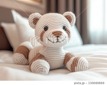 Cute crochet teddy bear lying on a bed with soft pillows in a cozy room background 130080669