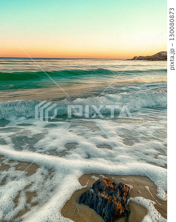 Sunset over tranquil beach with gentle waves lapping at the shore 130080873