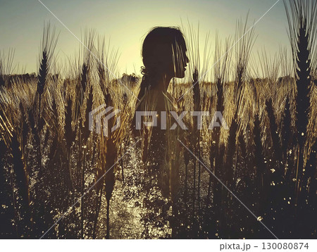 Silhouette of a woman standing in a wheat field during sunset near a rural area 130080874
