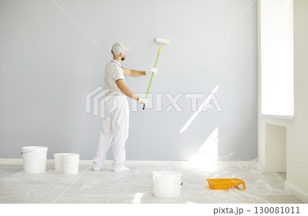 Professional male painter in white uniform painting light grey wall in bright room during renovation Professional male painter in white uniform painting light grey wall in bright room during renovation 130081011