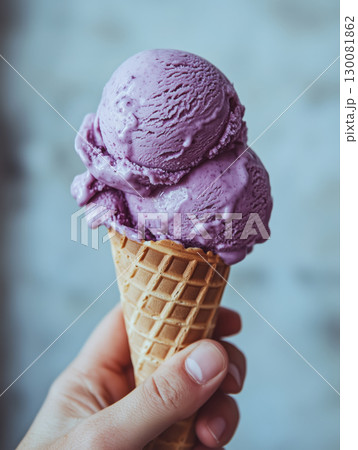 Close-up of hand holding purple ube ice cream in waffle cone against soft background. Sweet dessert concept. Close-up of hand holding purple ube ice cream in waffle cone against soft background. Sweet dessert concept. 130081862
