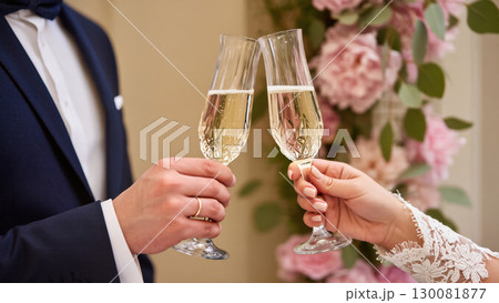 Close-up of bride and groom clinking champagne glasses during wedding celebration with floral background 130081877