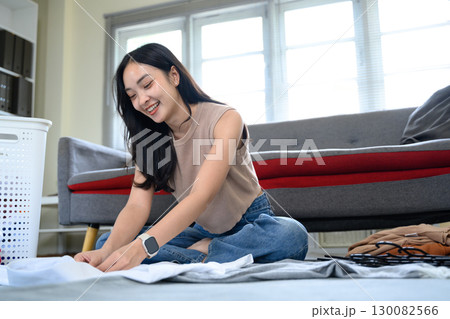 Cheerful female doing household chores, organizing clean clothes in living room 130082566