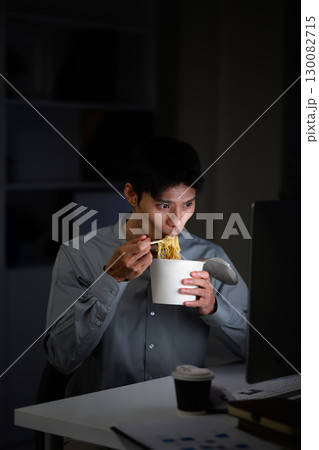 Asian businessman eating instant noodles while working late night at office desk Asian businessman eating instant noodles while working late night at office desk 130082715