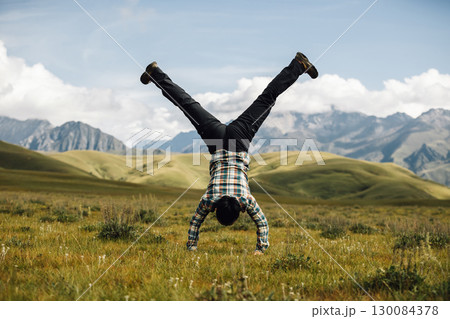 Woman hiker doing a handstand on high altitude mountain top grassland 130084378