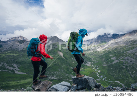 Two hiking friends climbing up to high altitude mountain top Two hiking friends climbing up to high altitude mountain top 130084480