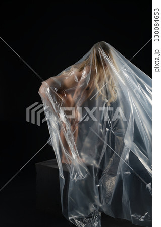 Blonde woman gracefully poses in studio wrapped in translucent plastic Blonde woman gracefully poses in studio wrapped in translucent plastic 130084653