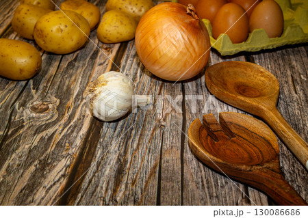 Overhead shot of an onion, garlic, potatoes, and wooden spoons, with a carton of eggs, arranged on a rustic wooden surface. Overhead shot of an onion, garlic, potatoes, and wooden spoons, with a carton of eggs, arranged on a rustic wooden surface. 130086686