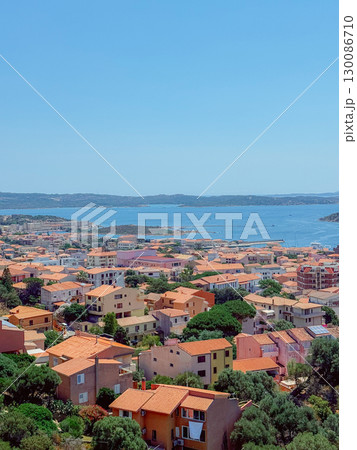 A stunning townscape showcasing charming buildings with red tiled roofs nestled by the coastline. The expansive view includes vivid blue waters and distant islands under a clear sky. Sardinia A stunning townscape showcasing charming buildings with red tiled roofs nestled by the coastline. The expansive view includes vivid blue waters and distant islands under a clear sky. Sardinia 130086710