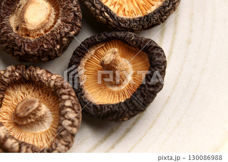 Dried shiitake mushrooms on kitchen ceramic plate. Raw dehydrated ingredient. Macro shot.  130086988