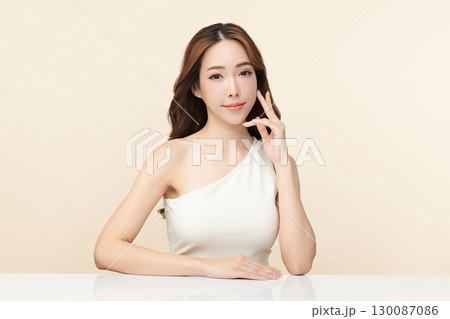 A beautiful young Asian woman with clean, fresh skin against a beige background. Skincare, facial treatment, cosmetology, beauty, and spa. An elegant portrait of an Asian woman. 130087086