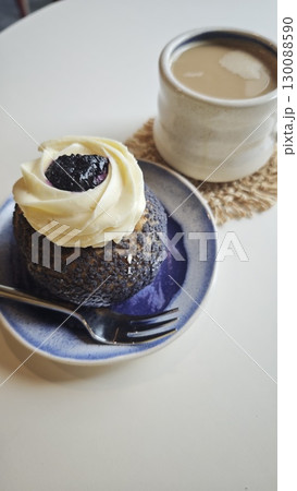 Blueberry dessert with cream frosting served on a ceramic plate next to a cup of coffee with milk 130088590