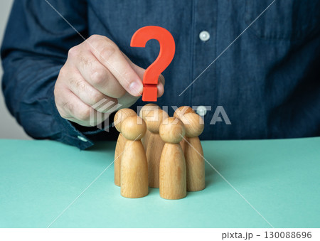 A man holds a question mark over a group of people figurines. To set the agenda. To find out the opinion of the team. To confuse the people and create uncertainty A man holds a question mark over a group of people figurines. To set the agenda. To find out the opinion of the team. To confuse the people and create uncertainty 130088696