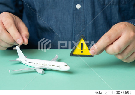 A man holds a sign of attention near a passenger plane. Some problems or malfunctions that risk canceling the flight, causing delays and safety concerns A man holds a sign of attention near a passenger plane. Some problems or malfunctions that risk canceling the flight, causing delays and safety concerns 130088699
