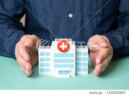 A man protects a hospital building with his hands. Concept of protecting the healthcare system. Medical security, patient safety, public health protection A man protects a hospital building with his hands. Concept of protecting the healthcare system. Medical security, patient safety, public health protection 130088865