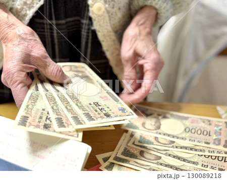通帳の前でたくさんの1万円札を数える高齢女性の手元 通帳の前でたくさんの1万円札を数える高齢女性の手元 130089218