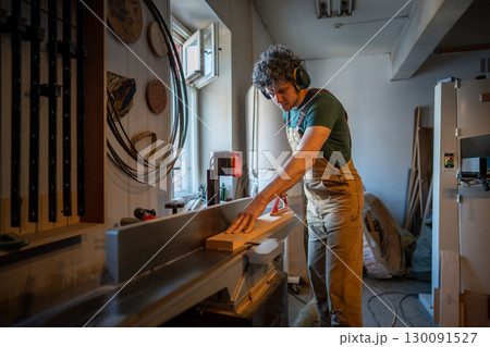 Skilled woodworker operate jointer machine, process wooden beam with power tools in workshop Skilled woodworker operate jointer machine, process wooden beam with power tools in workshop 130091527