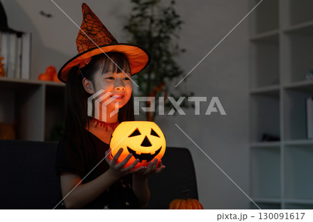 Halloween Spirit. Young girl in a witch hat holding a glowing pumpkin lantern. 130091617