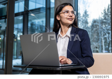 Dark-haired woman in eyeglasses working on laptop and looking confident 130091975