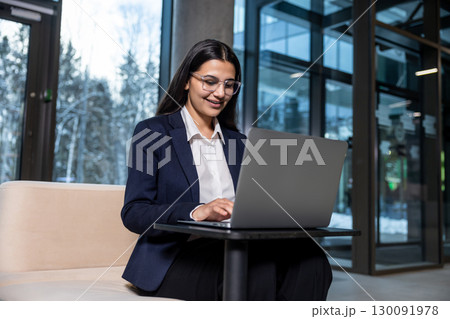 Dark-haired woman in eyeglasses working on laptop and looking confident 130091978