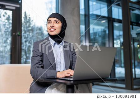 Muslim businesswoman in hijab working on laptop and looking involved 130091981