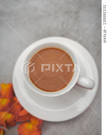Steaming cup of coffee with orange rose petals on marble table for autumn season 130092332